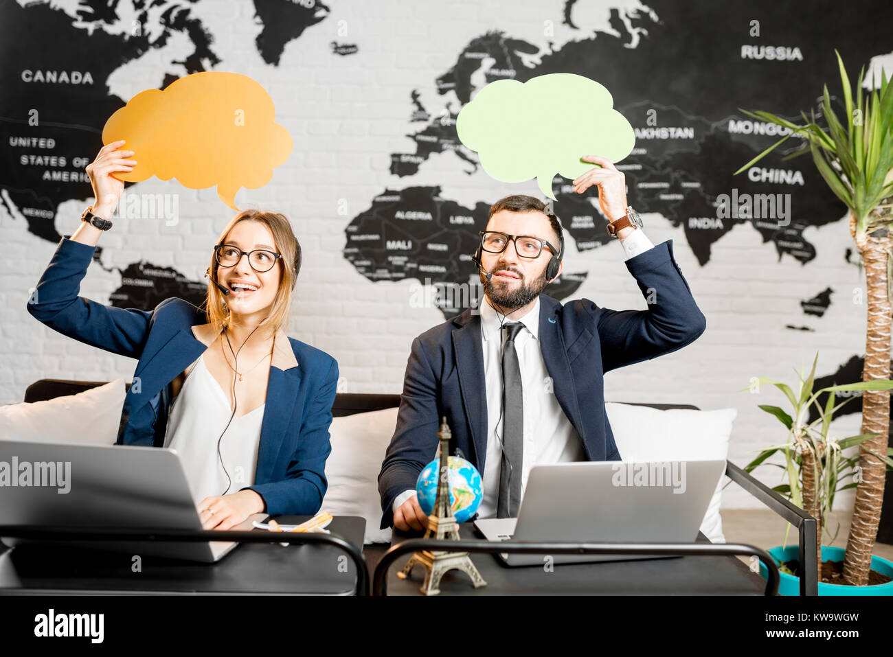 Couple of travel managers dreaming with colorful bubbles above the head sitting at the agency office with world map on the background Stock Photo