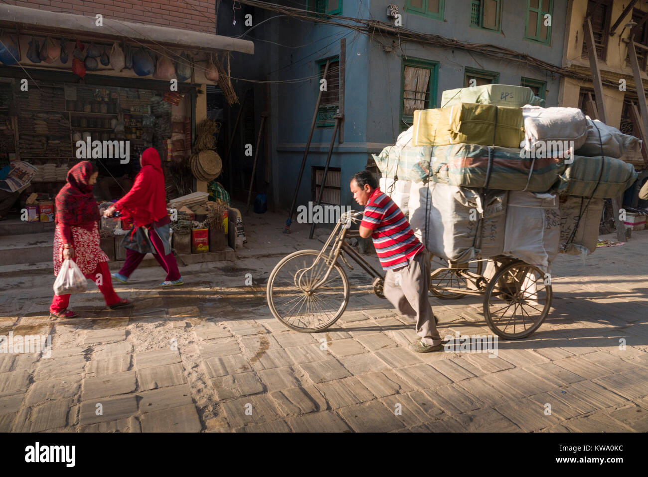 Man pushes tricycle loaded with cargo along dusty street of Kathmandu, Nepal Stock Photo