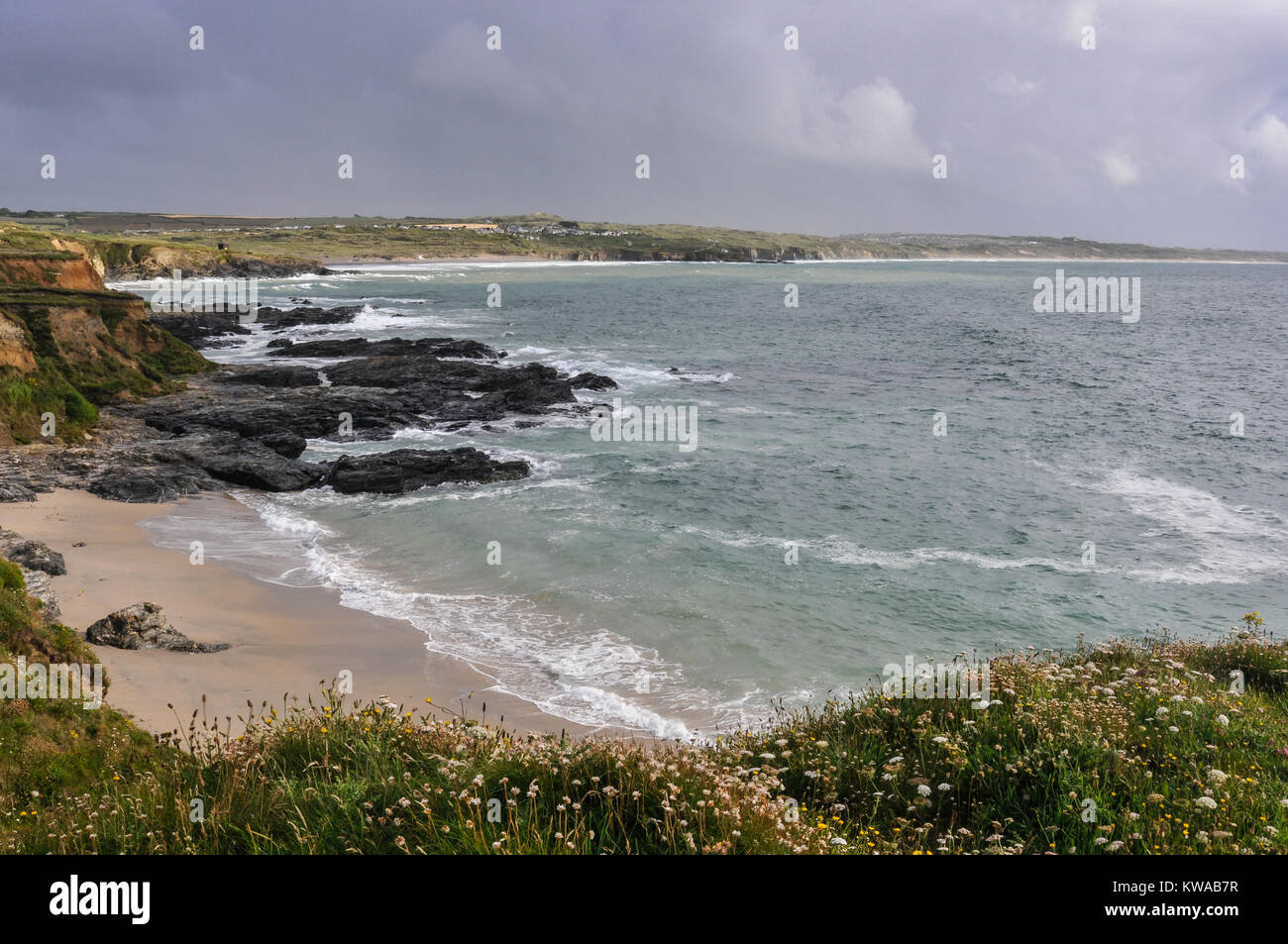 View out to sea from the grassy clifftop across a bay to the rocky beach on the Cornish coast, Cornwall, England, UK Stock Photo