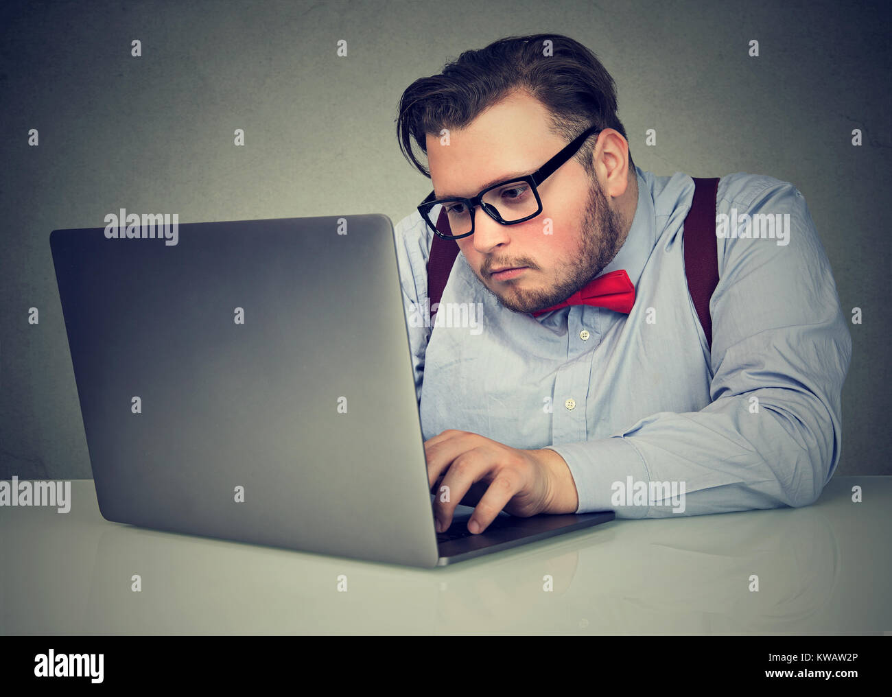 Young serious man in eyeglasses looking at laptop working diligently. Stock Photo