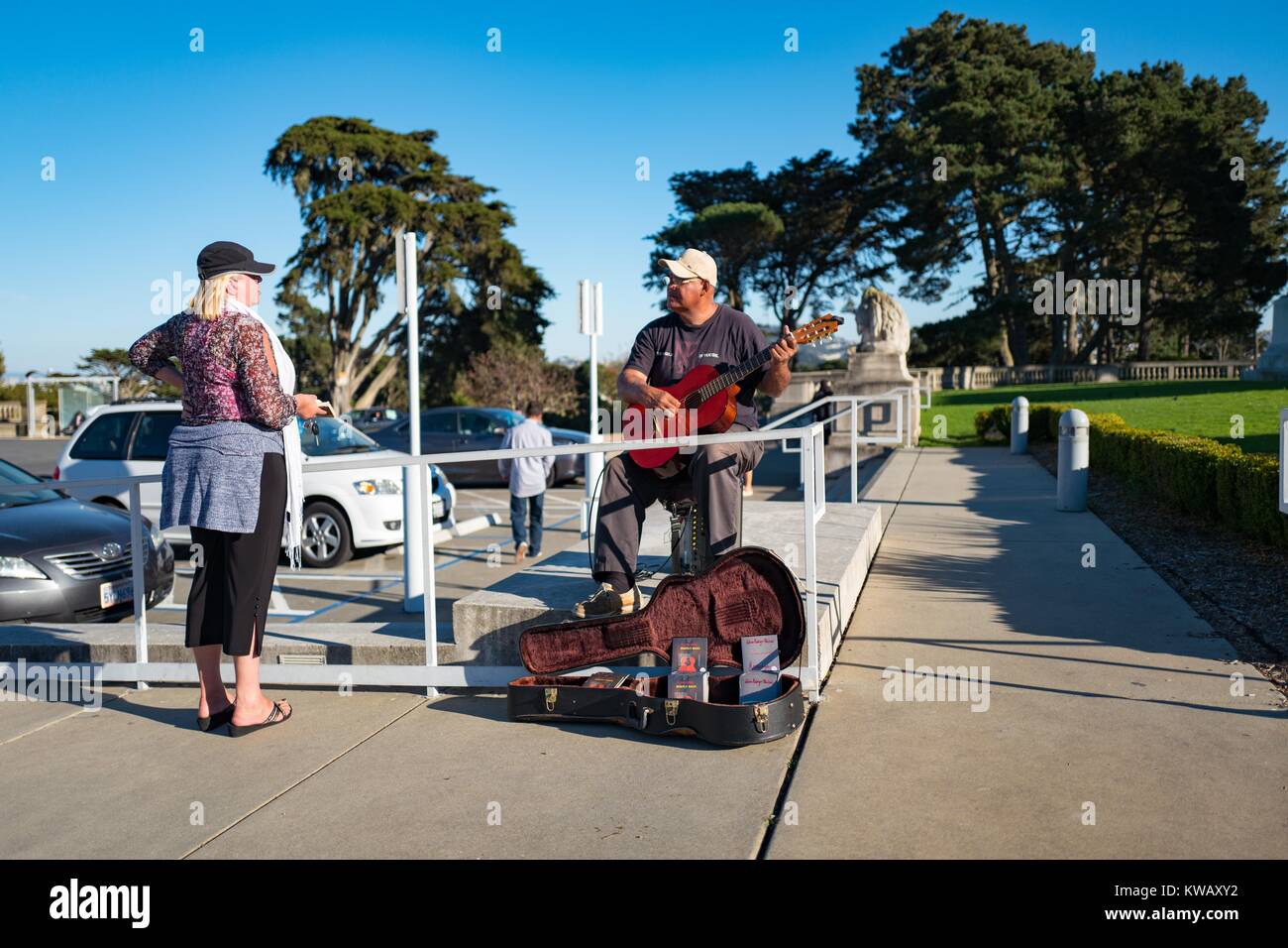 A woman pauses and speaks with a man who plays a guitar while busking in front of the California Palace of the Legion of Honor in the Lands End neighborhood of San Francisco, California, October 8, 2016. Stock Photo