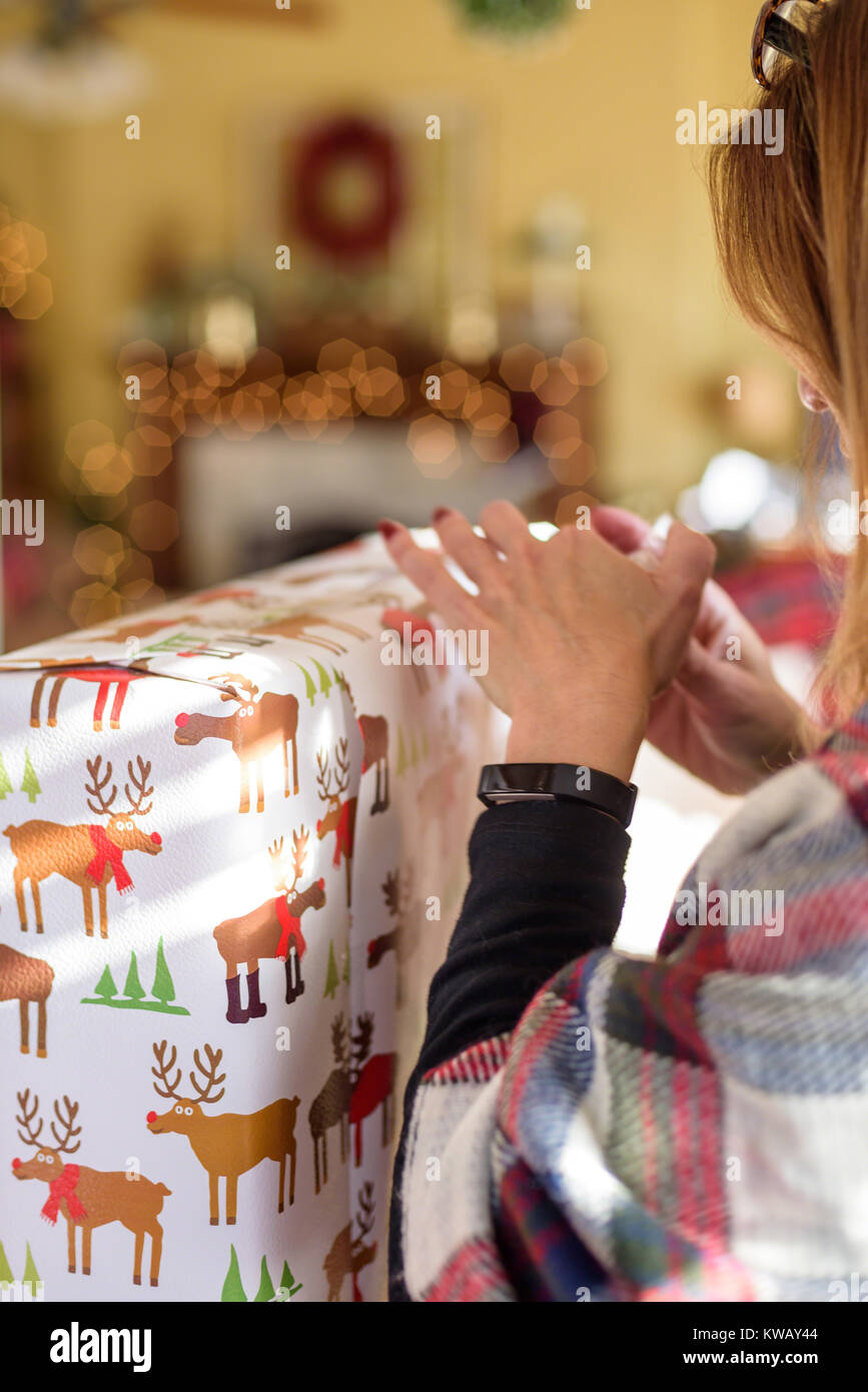 woman wrapping Christmas gift at home with bokeh lights in background Stock Photo