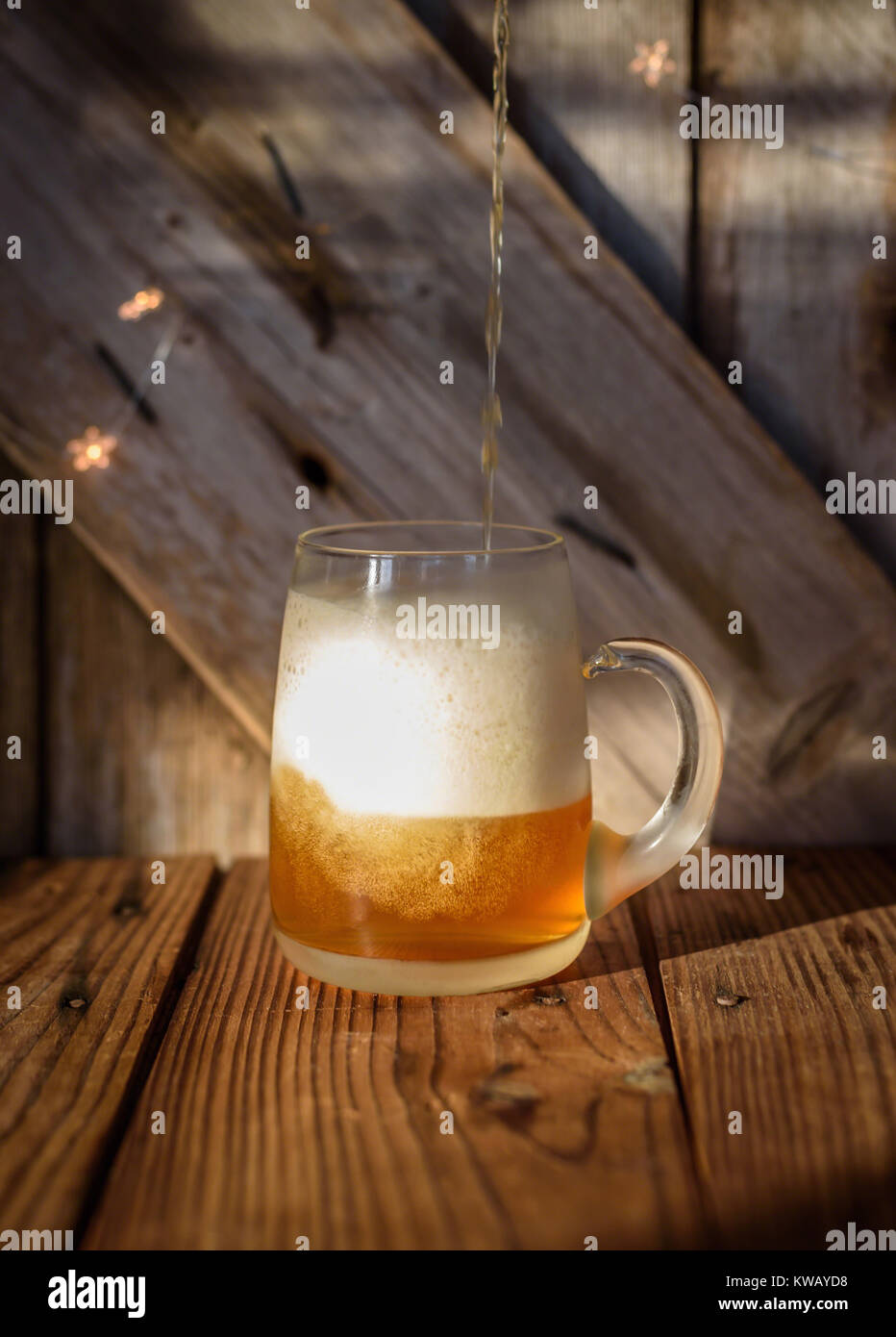 pouring beer into a large frosty beer mug on rustic barn wood table Stock Photo
