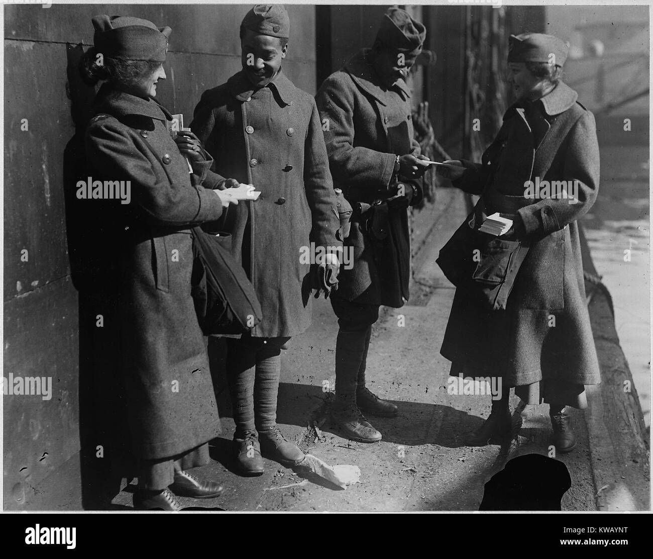 Dressed in long wool coats and hats, two female volunteers for the Salvation Army, known as 'donut lassies, ' hand out donuts to two returned African American soldiers of the 351st Field Artillery, Louisville, Kentucky, 1919. Image courtesy National Archives. Stock Photo