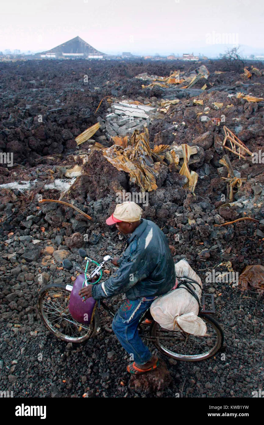 Mike Goldwater  / Network Photographers  This man cycles along a makeshift road that has been made across the cooling lava following the volcanic eruption that devasted about a third of the town of Goma.  In the backgroud is all that remains of the town's cathederal.   Jan 2002 Stock Photo
