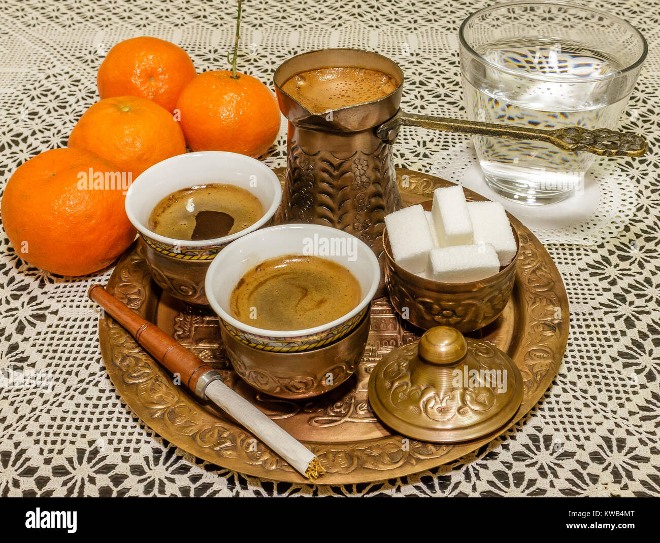 Turkish coffee served with a coffee pot,sugar cubes and glass of water with tangerines and cigarette holder on white doily Stock Photo