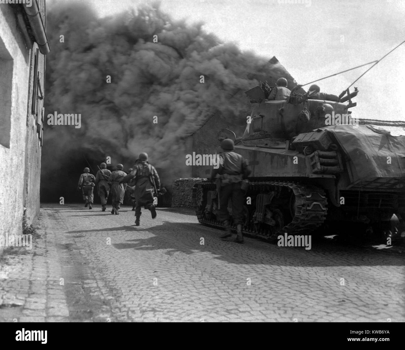 U.S. infantrymen running through the smoke-filled streets of Wernberg, Germany. 55th Armored Infantry Battalion and tank of the 22nd Tank Battalion. April 22, 1945. World War 2. (BSLOC 2014 8 78) Stock Photo