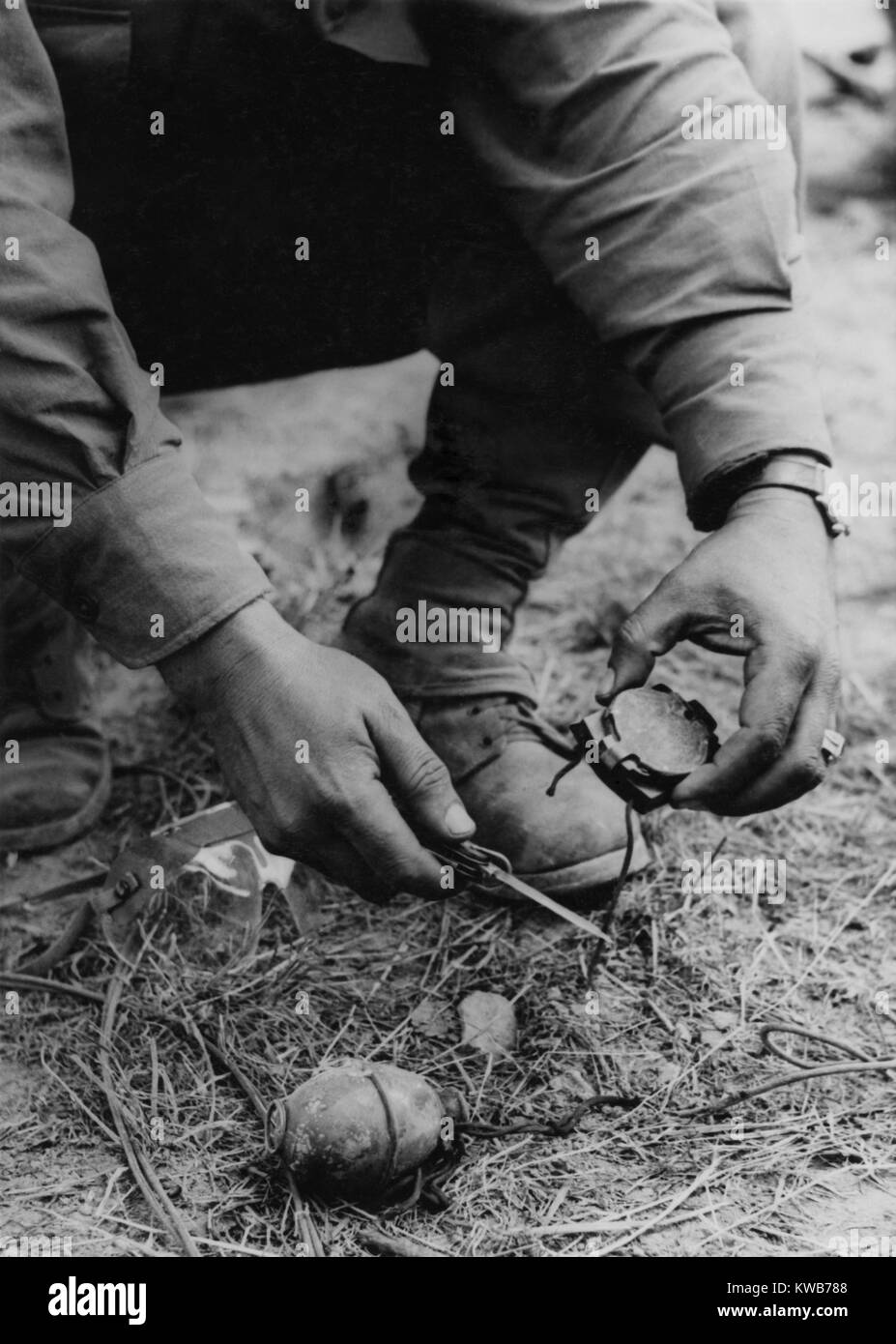 U.S. soldier dismantles a German booby trap planted on the road to St. Gilles. The device consisted of a tempting compass attached to a grenade with a shoestring. Picking up the compass would have pulled a pin, setting off the grenade. 1944. World War 2. (BSLOC 2014 10 159) Stock Photo