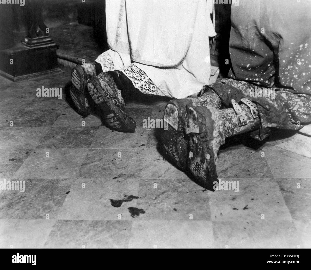 With soiled army boots, a Chaplain and soldier kneel at Catholic Mass is held for two dead soldiers. Oct. 11, 1944. San Benedetto, Italy. World war 2. (BSLOC_2014_10_51) Stock Photo