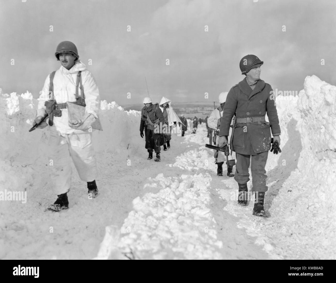 U.S. soldiers patrol on a path plowed through snow in the Ardennes during the Battle of the Bulge. Some infantry men have full white uniforms while others have only partial or no camouflage covering. Ca. Dec. 26, 1944 through Jan. 25, 1945. World War 2. (BSLOC 2014 10 93) Stock Photo