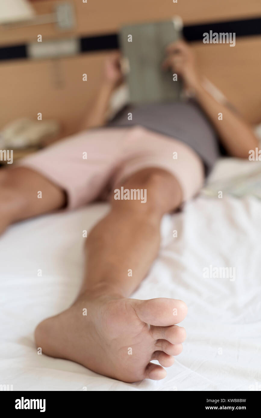 closeup of a young caucasian man wearing shorts using a digital tablet or an e-reader in bed Stock Photo