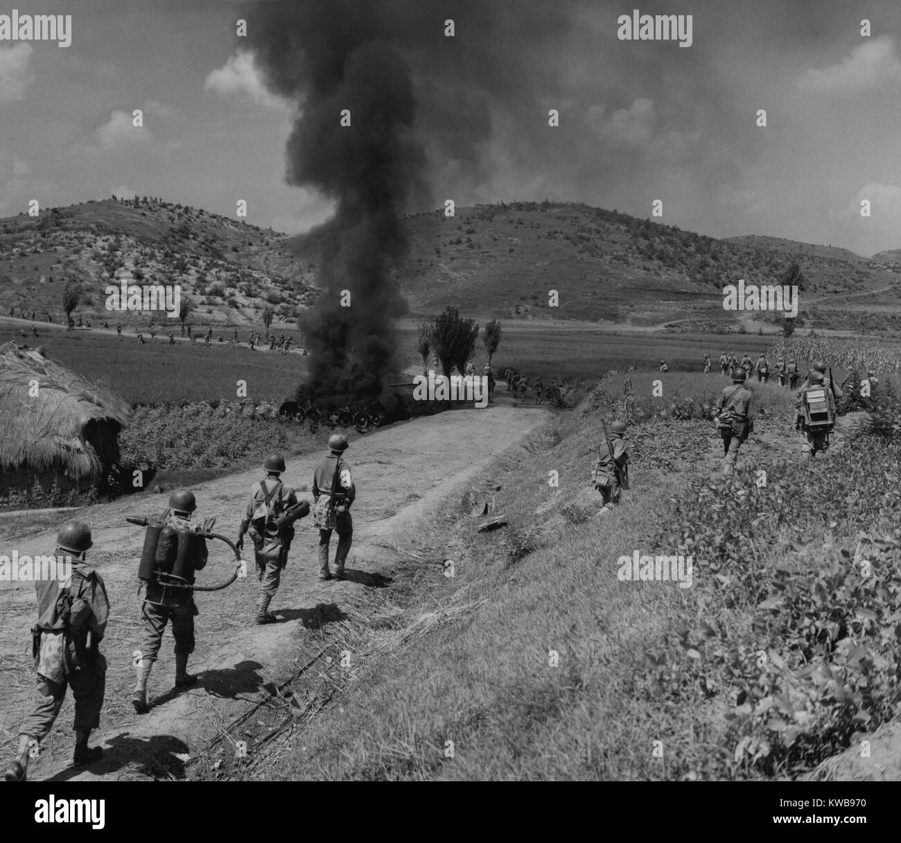 U.S. Marines advancing in the Naktong River Battle, Sept. 4, 1950. The men in the column are spaced out to avoid casualties and walk around the burning North Korean tank. Second from left Marine carries a flame thrower, and the man in front of him has a rocket launcher. Battle of Pusan Perimeter. Korean War, 1950-53. (BSLOC 2014 11 25) Stock Photo