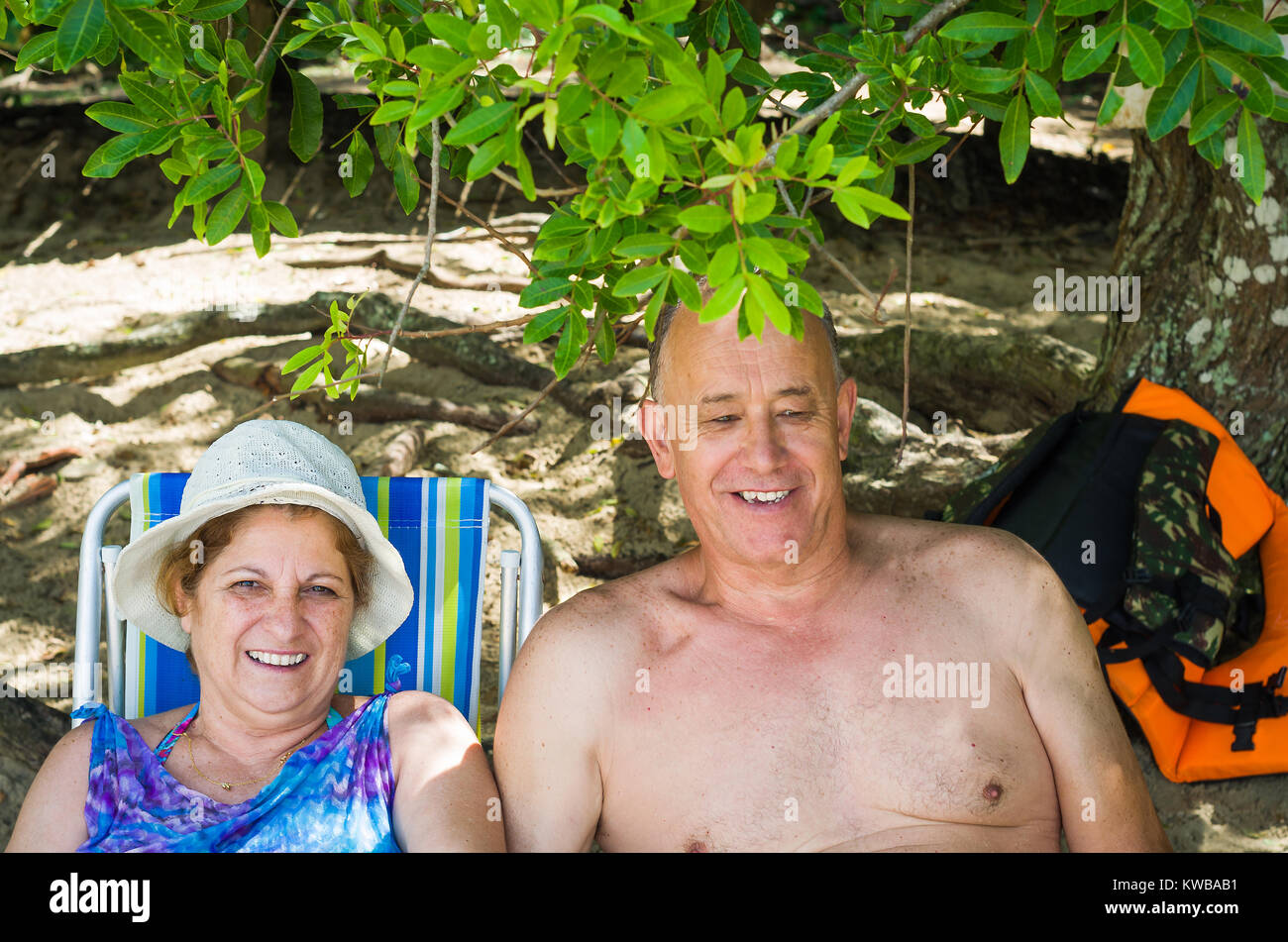 Old couple laughing on the beach, sitting, love. Stock Photo