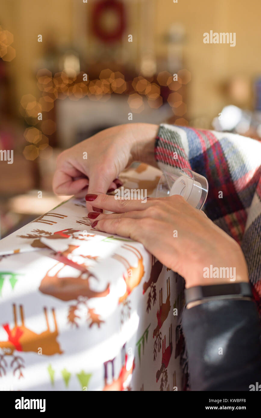 closeup of woman wrapping Christmas gift at home with fireplace and bokeh lights in background Stock Photo