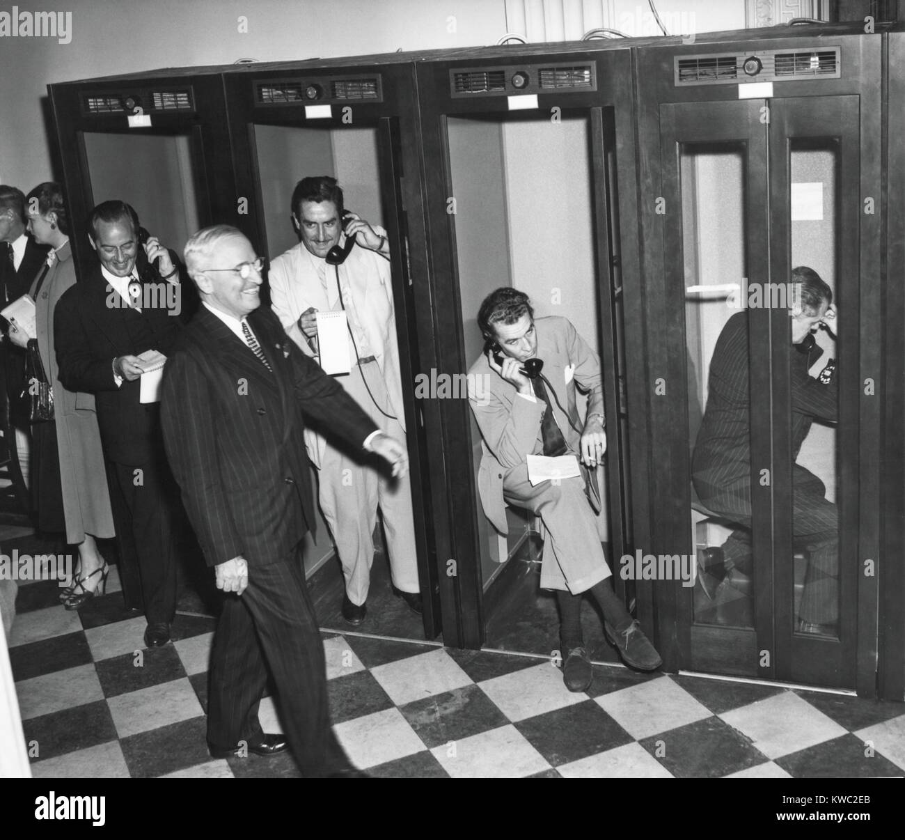 President Harry Truman walks past reporters in the telephone booths the Old State Department Building. They are reporting back to their headquarters after Truman's press conference, April 27, 1950. It was the first conference to require newsmen to remain seated and arise and identify themselves when asking questions. (BSLOC_2015_2_238) Stock Photo