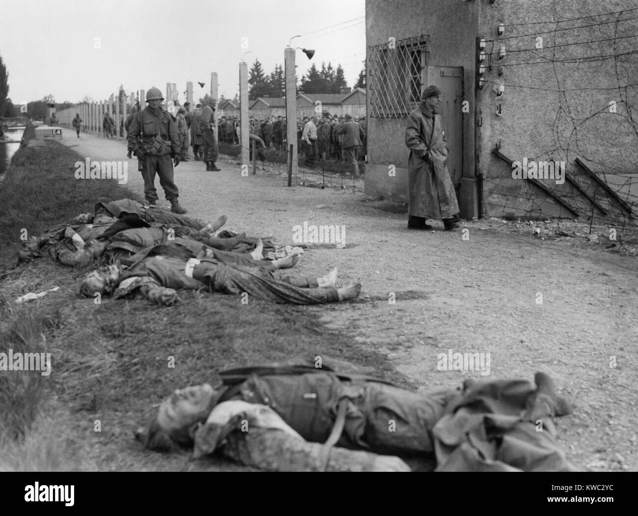 Bodies of former SS guards lie on the bank of a moat surrounding the Dachau Concentration Camp. Liberated prisoner's killed the guards by beating them to death. Seventh US Army soldiers patrolled the area and checked liberated prisoners in the barbed wire enclosure. April 29, 1945, World War 2 (BSLOC_2015_13_15) Stock Photo