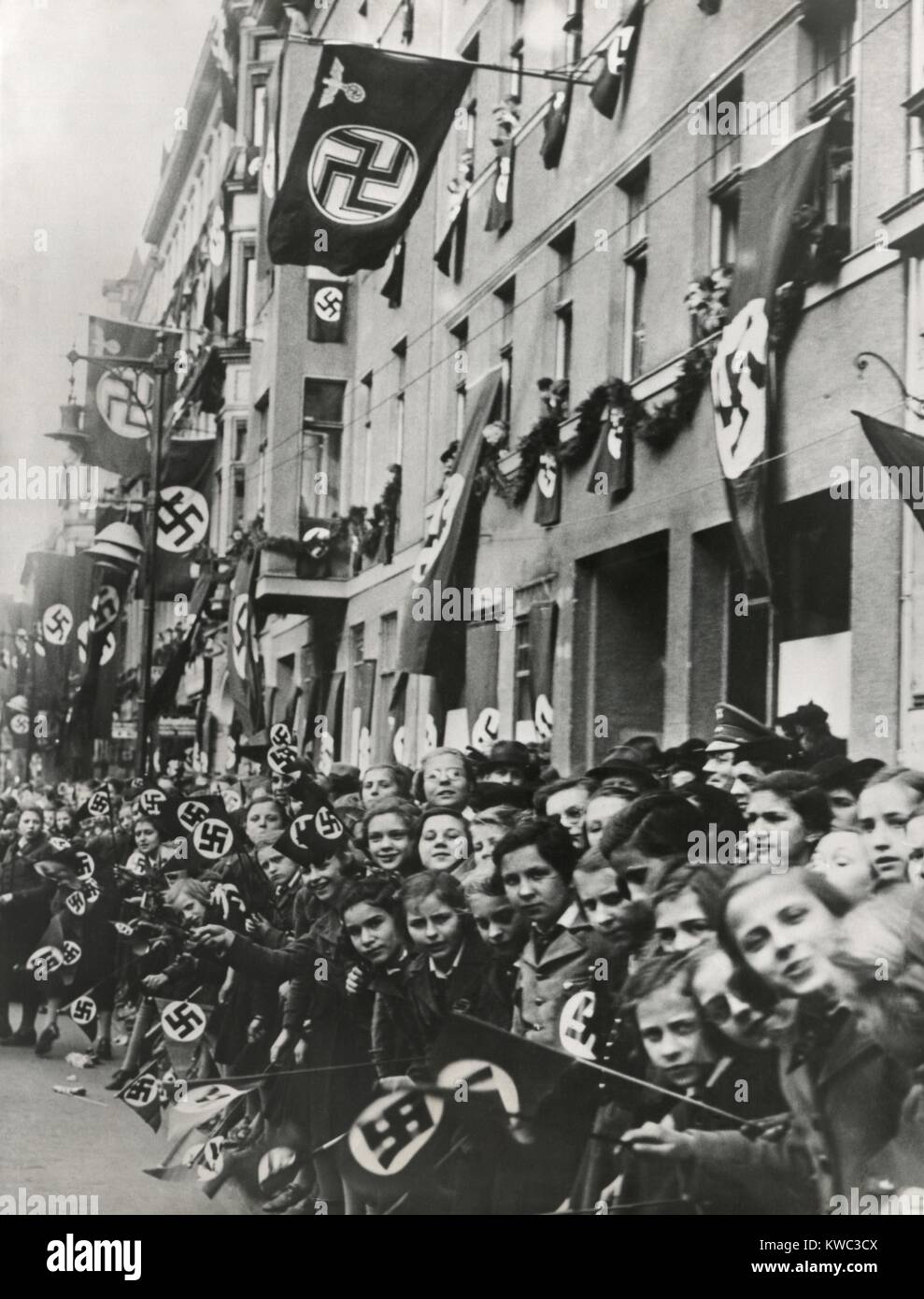 German children equipped with swastika flags look toward an advancing Nazi parade. Ca. 1935-1939. Unidentified location. (BSLOC 2015 13 50) Stock Photo