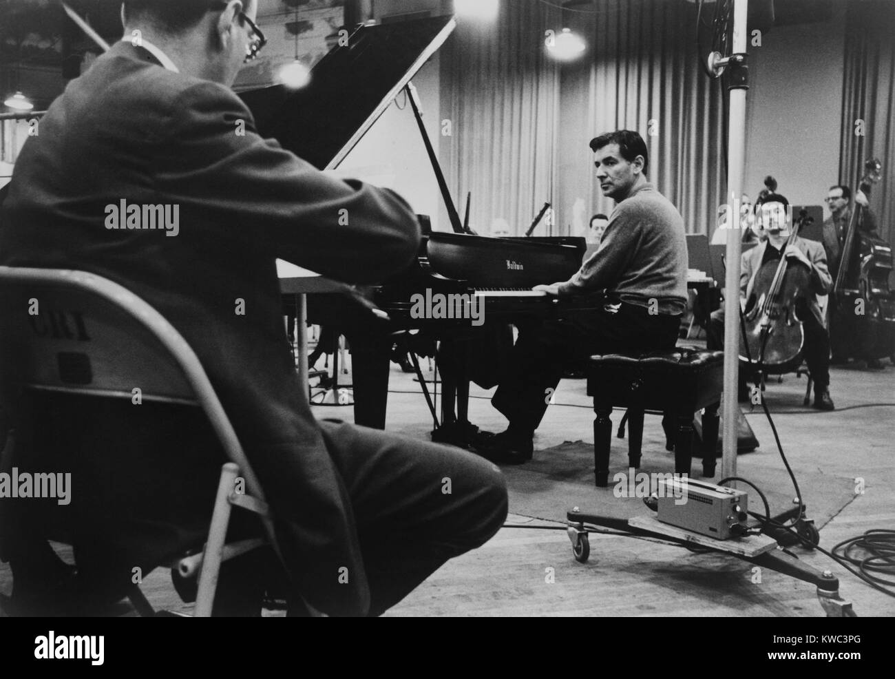 Leonard Bernstein, playing piano, amidst other musicians during a rehearsal  in 1958. (BSLOC 2015 14 164 Stock Photo - Alamy