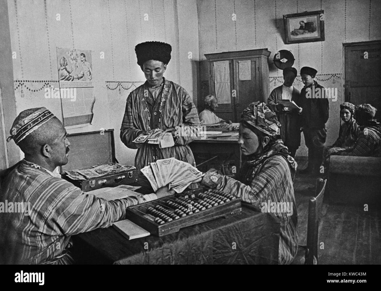 Turkmenian collective farmers receiving their share of yearly profits in the 1930s. The farm administrator calculates with an Abacus. Pictures of Stalin and Lenin hang on the walls. (BSLOC 2015 14 6) Stock Photo