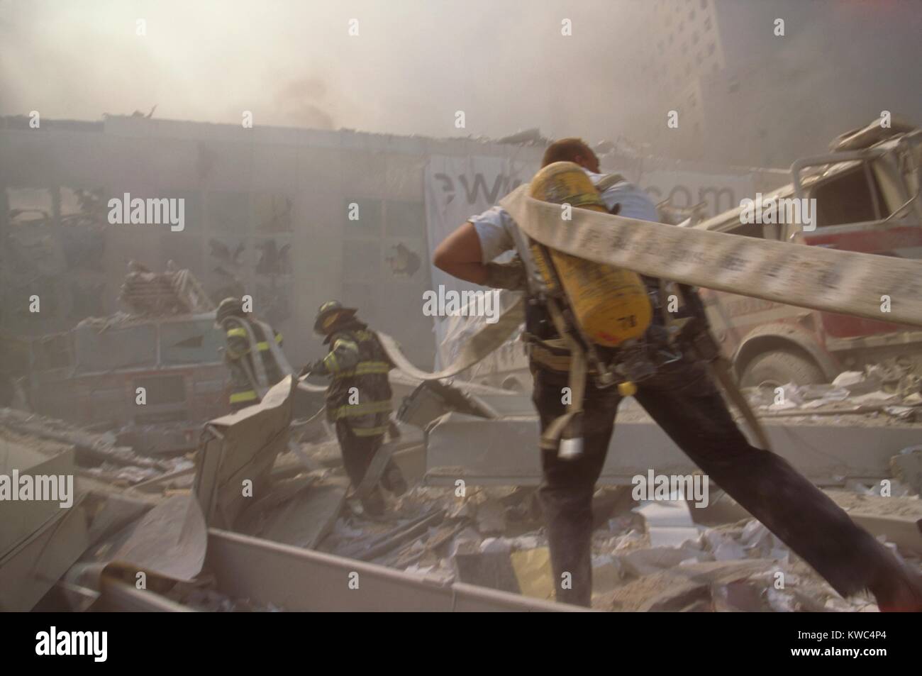 Fire fighters hauling a hose through rubble on September 11th, following terrorist attack on World Trade Center. The nearest structure is a pedestrian bridge over the West Side Highway (West St.) that connected the WTC 1 (North Tower) with the World Financial Center and Battery Park City. New York City, Sept. 11, 2001. (BSLOC 2015 2 45) Stock Photo