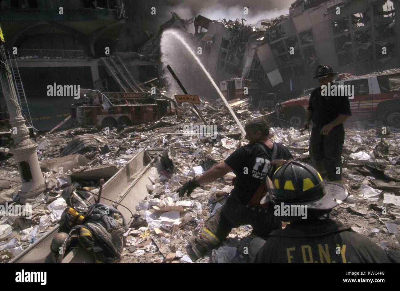 Fire fighters set up a hose amid smoking rubble following September 11th terrorist attack on World Trade Center. At left is still standing WTC 6. At right is the destroyed North pedestrian bridge over West Side Highway (West St.). The water stream is aimed in-between, toward the burning pile of the collapsed WTC1 (North Tower). New York City, Sept. 11, 2001. (BSLOC 2015 2 49) Stock Photo