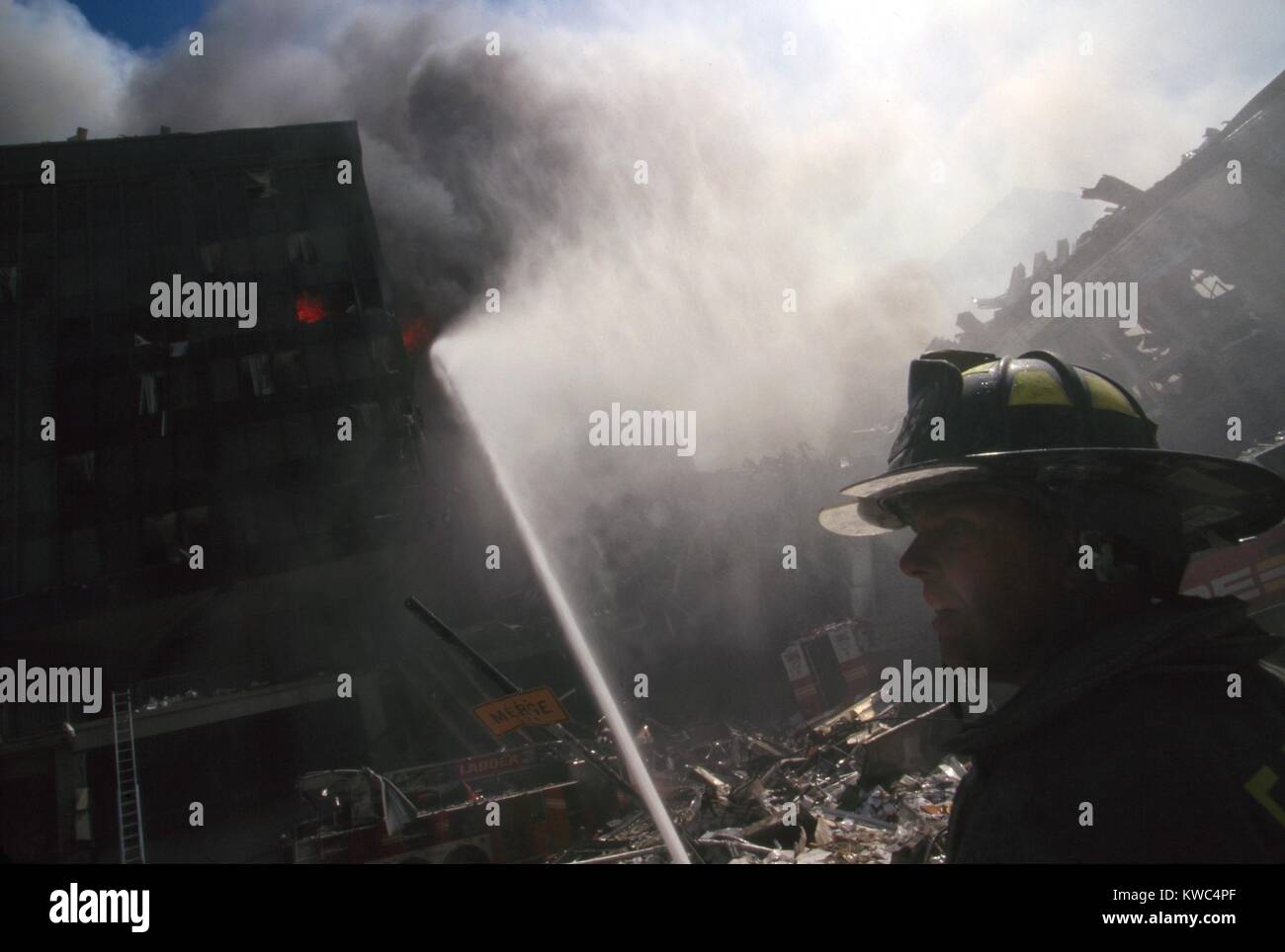 Fire fighter at World Trade Center site following September 11th terrorist attack. In the center background is the burning pile of the collapsed WTC 1 (North Tower). New York City, Sept. 11, 2001. Burning at left is the still standing WTC 6. At far right is the destroyed North pedestrian bridge over West Side Highway (West St.). (BSLOC 2015 2 55) Stock Photo