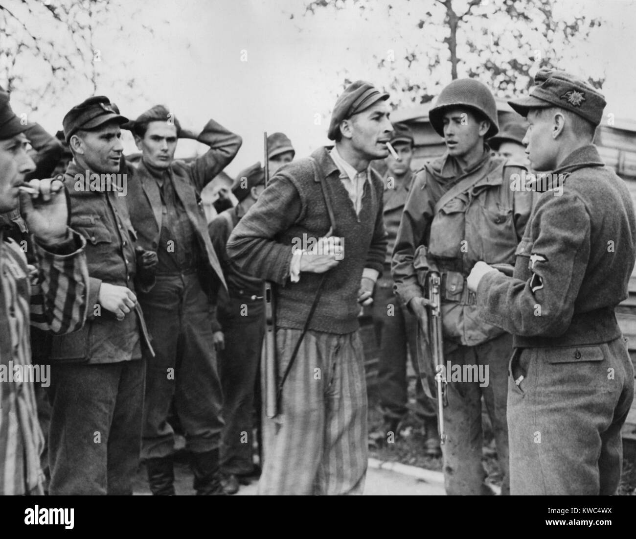 Freed Polish prisoner (center) of Dachau confronts a Nazi SS trooper for mistreatment of inmates. Still wearing his the striped trousers of his prison uniform, he has a rifle slung over his shoulder. A soldier of the Seventh US Army stands by. April 29, 1945, World War 2 (BSLOC 2015 13 14) Stock Photo