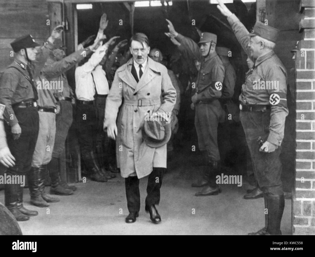 Adolf Hitler, emerging from a Nazi party meeting after a speech, 1930s. He is saluted by uniformed Storm Troopers. Hitler wears a business suit under his trench coat, suggesting the photo was taken during his early chancellorship. (BSLOC 2015 13 54) Stock Photo