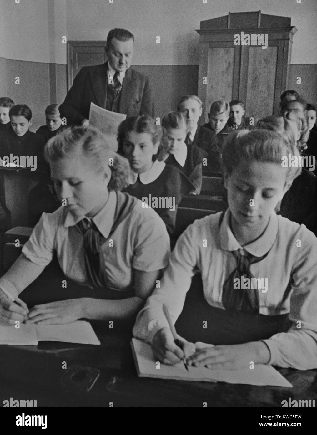 Young Pioneer girls sitting at the front desk in a Latvian USSR sixth grade classroom. They wear the red scarfed uniforms of the Communist youth organization in 1940. Latvia was forcibly incorporated into the Communist Soviet Union after the signing of the 1939 Nazi German-Soviet Non-Aggression Pact. (BSLOC 2015 14 8) Stock Photo