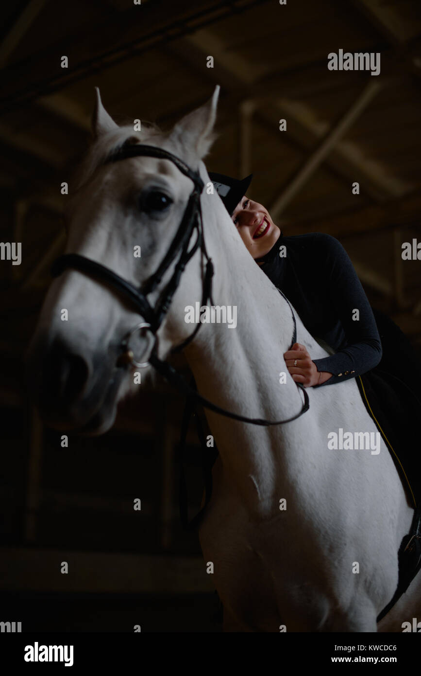 Smiling woman hugs horse neck sitting on it. Stock Photo