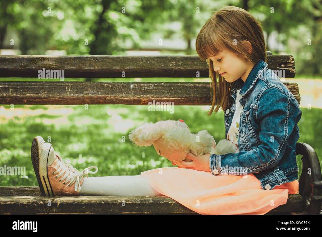 Happy little girl sitting on a bench in the park and holding in hands ...