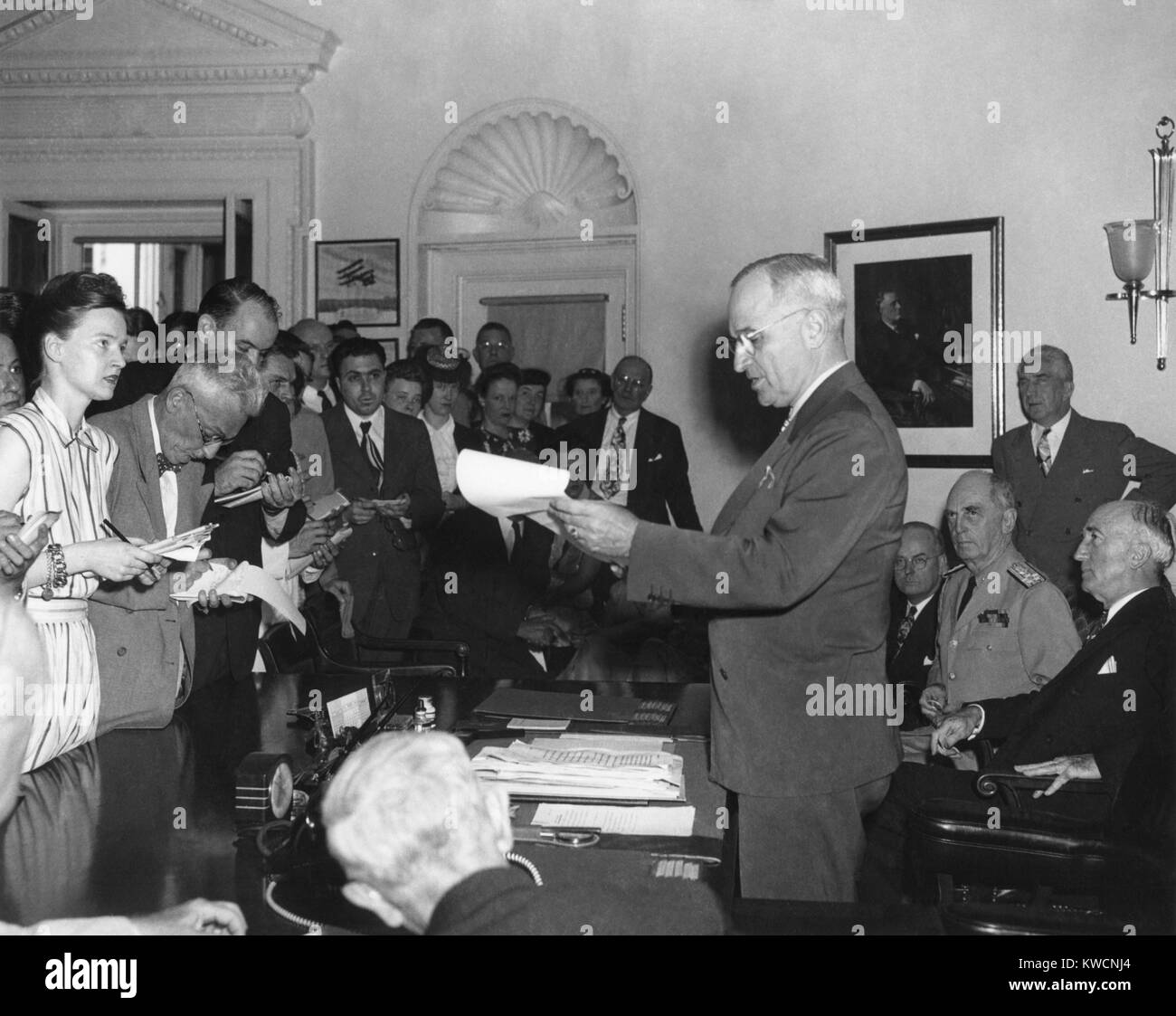 President Harry Truman announcing Japan's surrender to reporters in the Oval Office. Seated behind President Truman are John Snyder, Treasury Sec.; Adm. William Leahy; and Sec. of State James Byrnes. August 14, 1945. - (BSLOC 2014 15 19) Stock Photo
