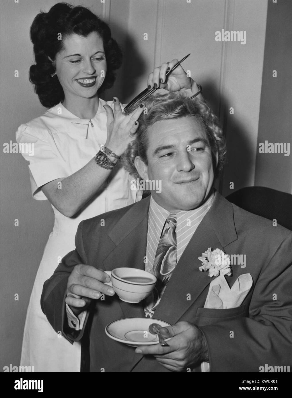 Wrestler Gorgeous George holding a tea cup as his hair is styled by Miss Bettie of Hollywood. Feb. 19, 1949. He appeared in the 1949 movie, ALIAS THE CHAMP. - (BSLOC 2014 17 162) Stock Photo