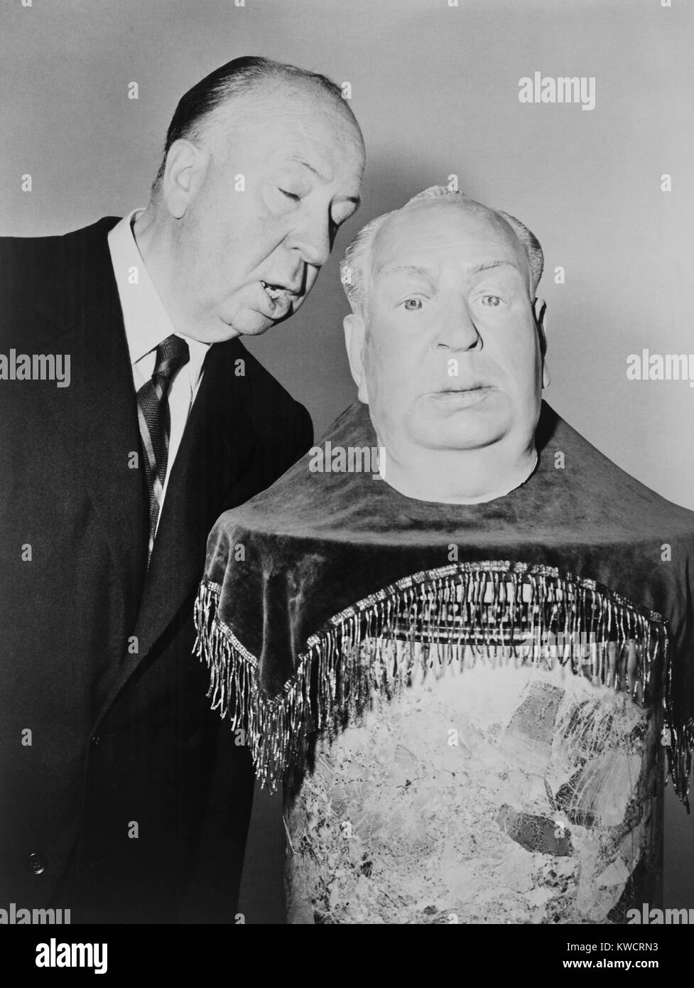 Alfred Hitchcock whispering into the ear of a plaster sculpture of his head. It will be his stand-in as he begins shooting the fourth TV season premiere of 'Alfred Hitchcock Presents.' Oct. 6, 1958. - (BSLOC_2015_1_20) Stock Photo