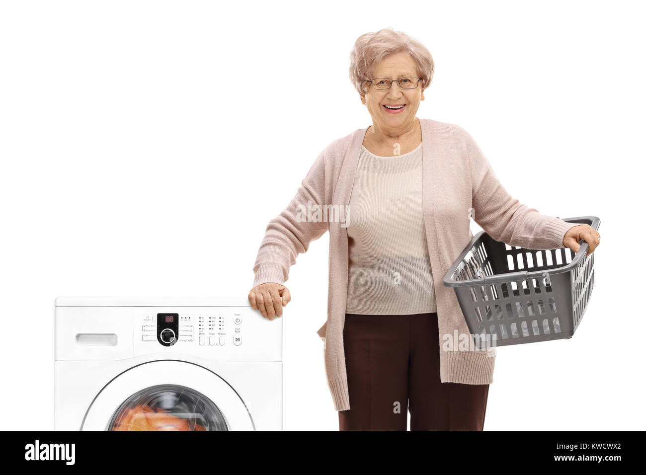 Elderly woman with an empty laundry basket next to a washing machine isolated on white background Stock Photo