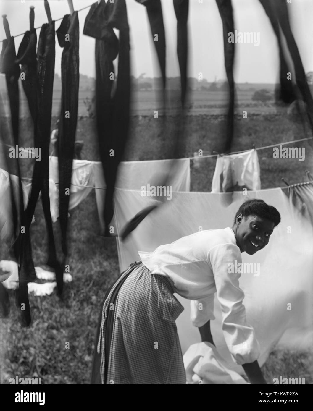 Informal portrait of a young African American woman surrounded by laundry in Newport, R.I. She is working in the midst of clotheslines holding sheets and stockings, in a 1902 photo by Gertrude Kasebier  (BSLOC 2017 20 107) Stock Photo