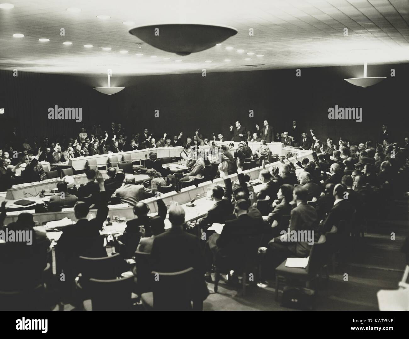 United Nations delegates, some wearing headphones with hands raised to ...