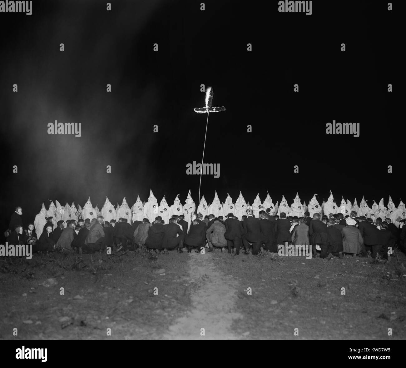 Ku Klux Klan gathering with fully robed and hooded members and kneeling men in face masks. There is a burning cross at what appears to an nocturnal initiation ceremony on June 28, 1922. Photo by National Photo Company and was likely taken within 100 miles of Washington, D.C. (BSLOC 2015 16 173) Stock Photo