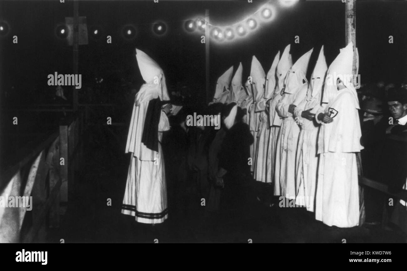 Four masked women kneeling in front of shrouded Klansman reading from a book. The Ku Klux Klan initiation ceremony took place on Long Island, New York in 1924. (BSLOC 2015 16 174) Stock Photo