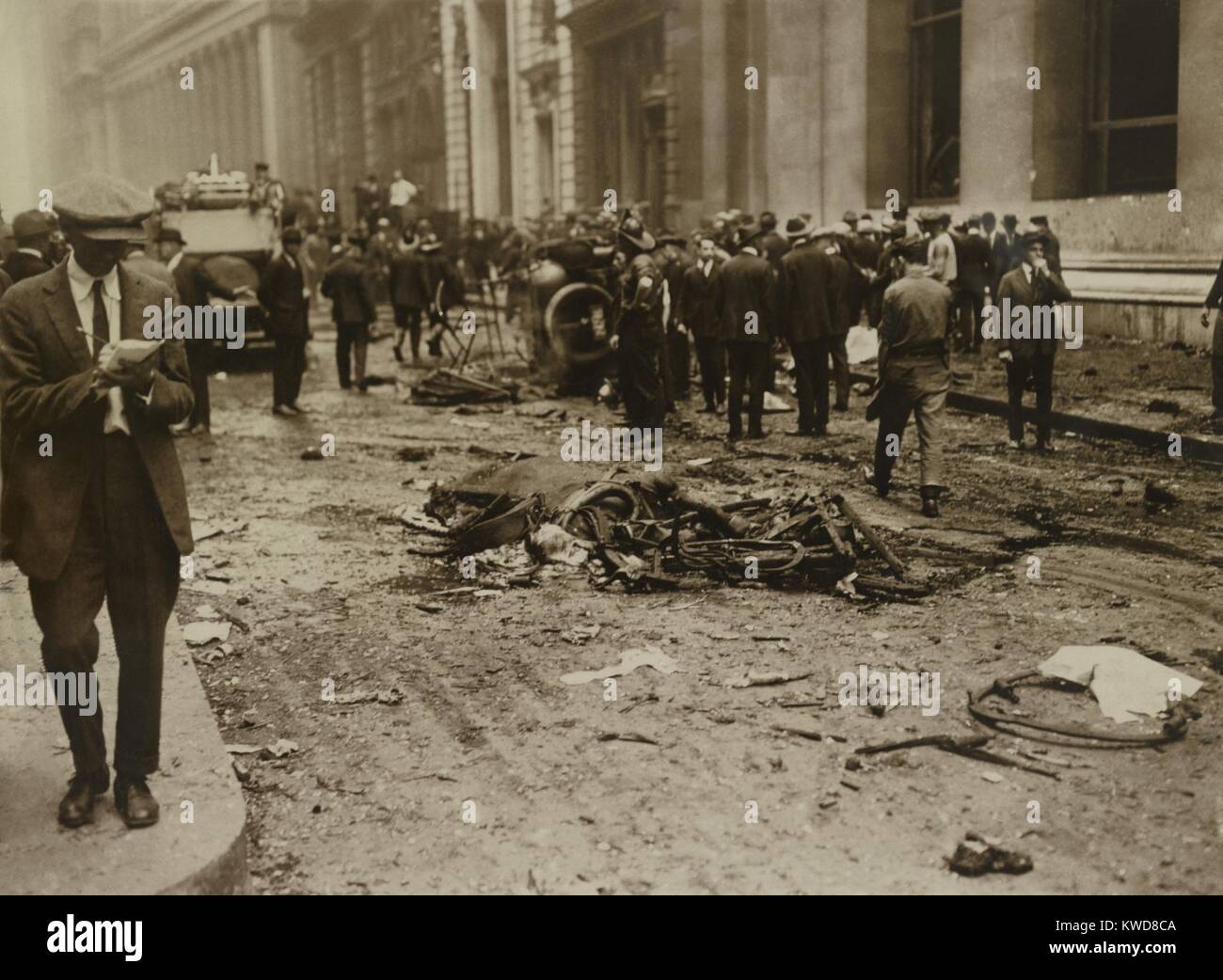 Crowd gathered behind a dead horse after the Wall Street Bombing, Sept. 16, 1920. The dead horse was the biggest clue to the bombing. When the New York Stock Exchange ordered an immediate clean up. it was removed and sent away to be 'ground into paste.' At left, a New York City reporter walks as he writes notes. The Morgan Bank is at right. (BSLOC 2015 17 238) Stock Photo