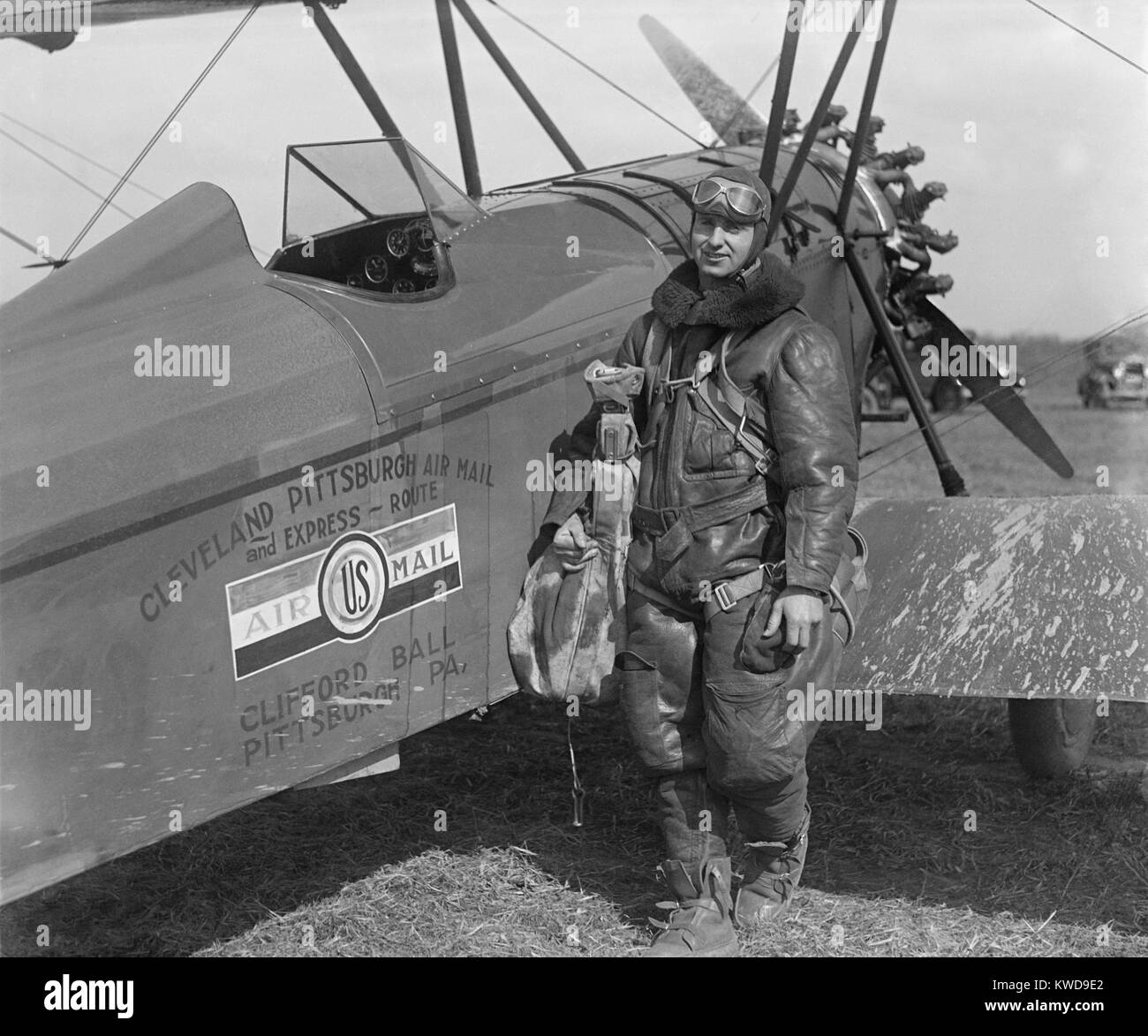 Aviator standing with plane labeled 'Cleveland Pittsburgh Air Mail and Express Route,' c. 1920-26. He is wearing a multi-layer cold weather flying suit and a parachute (BSLOC 2016 10 158) Stock Photo
