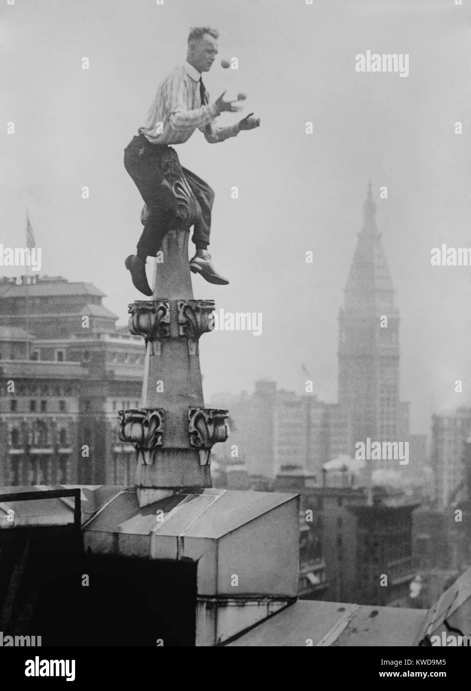 'Human Fly' John 'Jammie' Reynolds juggles while balancing atop a roof decoration in New York City. In the distance is the New York Life Building at the Madison Square Park. Ca. 1915-1920. (BSLOC 2015 17 169) Stock Photo