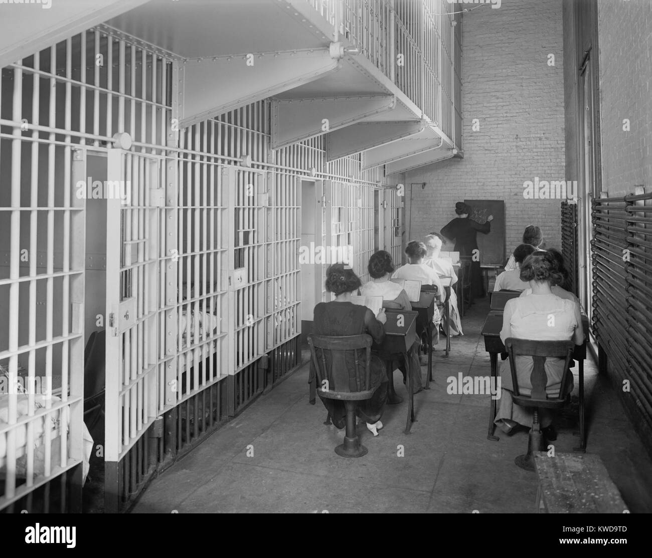 Young women at desks in an American jail c. 1920. Dressed in street clothing, they sit in two rows of desks in a cellblock. The teacher is writing numbers on the blackboard (BSLOC 2016 10 73) Stock Photo