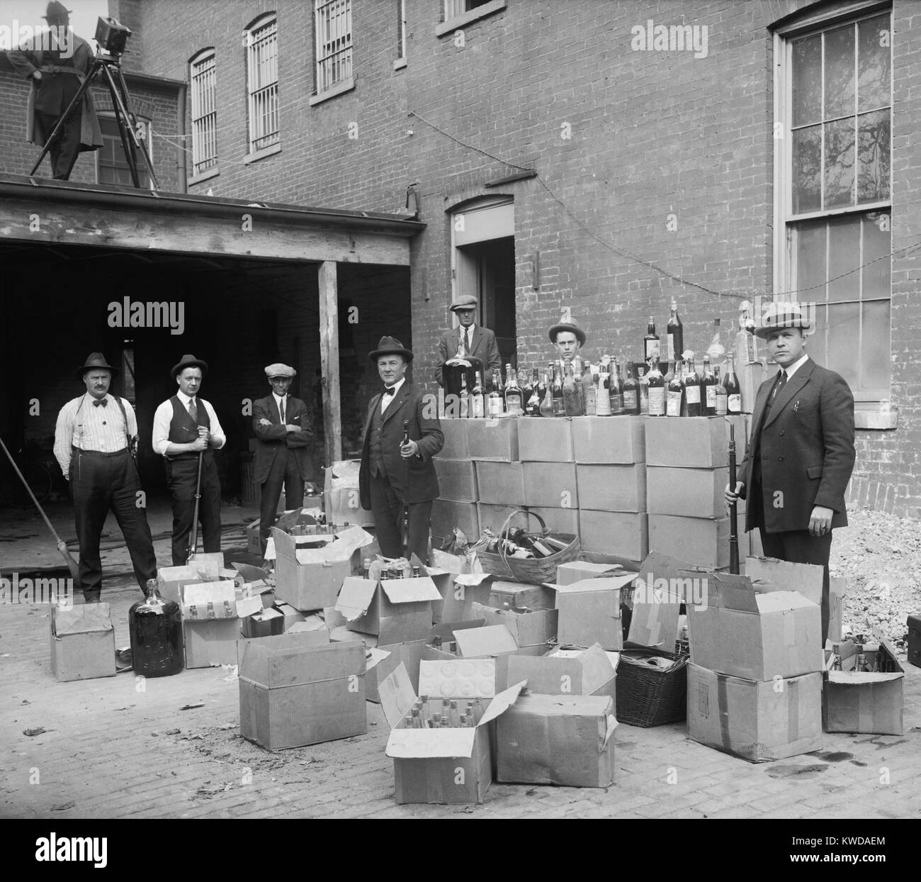 Prohibition agents stand with boxes and bottles of wine and liquor after a raid in Wash. D.C. area. Oct. 14, 1922. Note the camera man in upper left (BSLOC 2016 8 69) Stock Photo