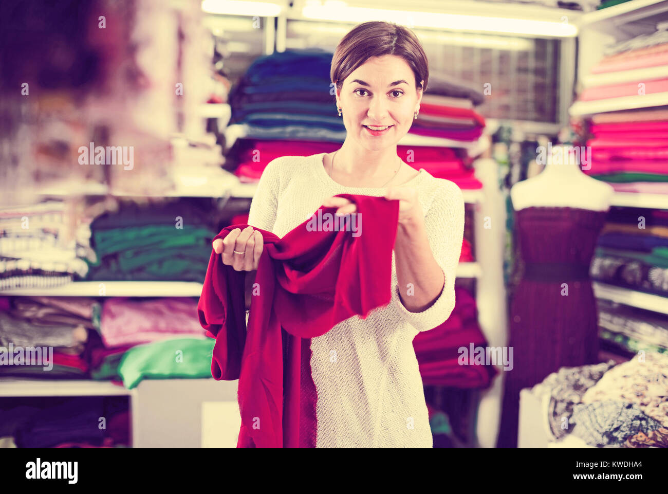 Young female shopper examining fabric quality for dress at drapery shop