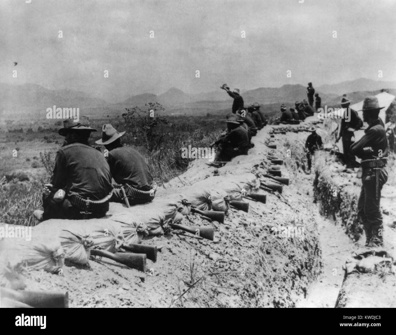 In the American trenches before Santiago during a truce, in July 1898. On the high ground above the city and harbor of Santiago, soldiers near trenches topped with sandbags and rifles ready for firing; one man standing in the center is waving his hat. Spanish American War in Cuba (BSLOC 2017 10 39) Stock Photo