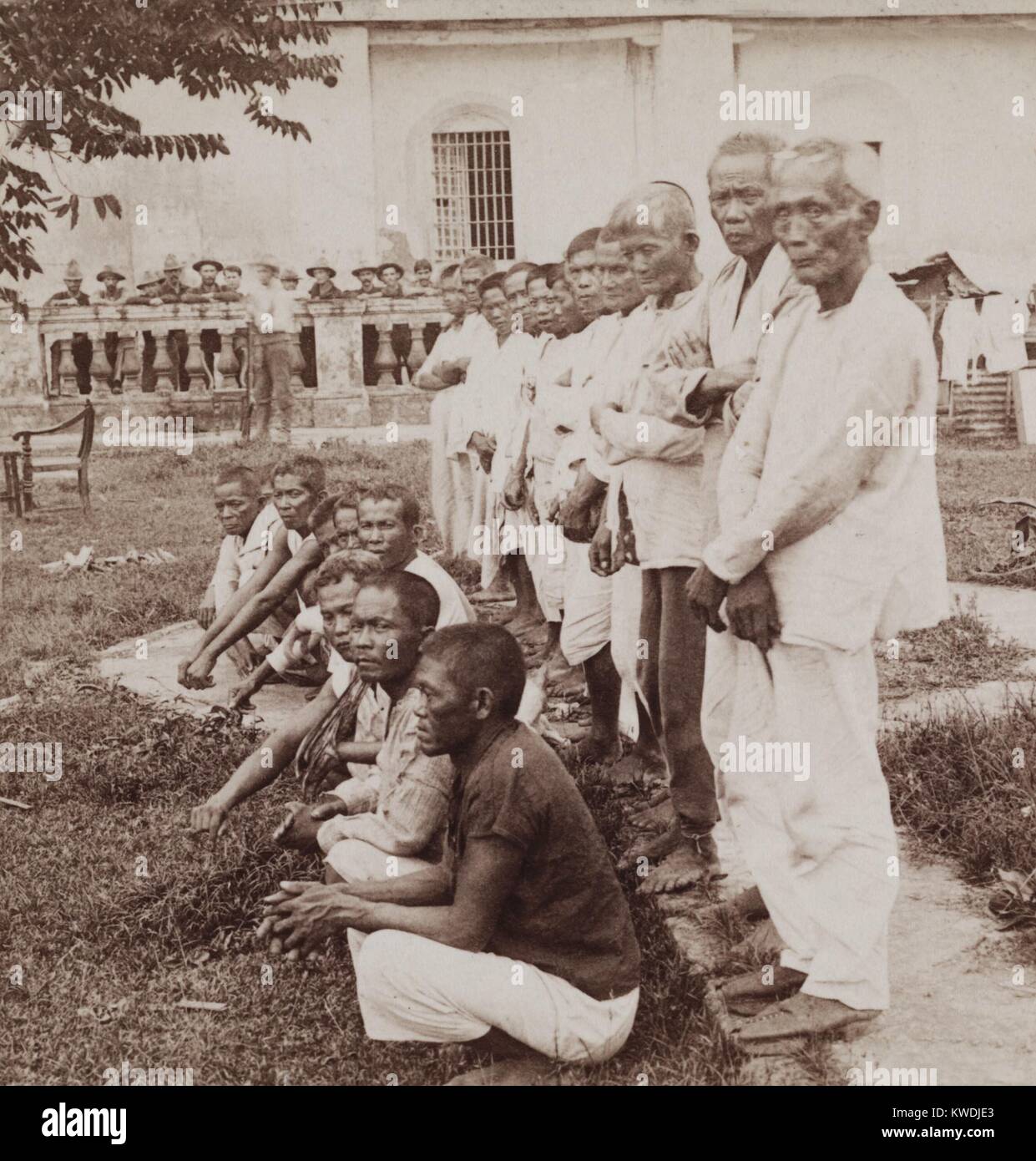 Filipino insurgents as prisoners of war at Pasig, Philippine Islands, 1899. These 19 men were some of 175 POWs taken in the March 14-15, 1899, in the first organized US campaign of the Philippine-American War, the 2nd Battle of Manilla. 12 American soldiers look on from then background (BSLOC 2017 10 79) Stock Photo