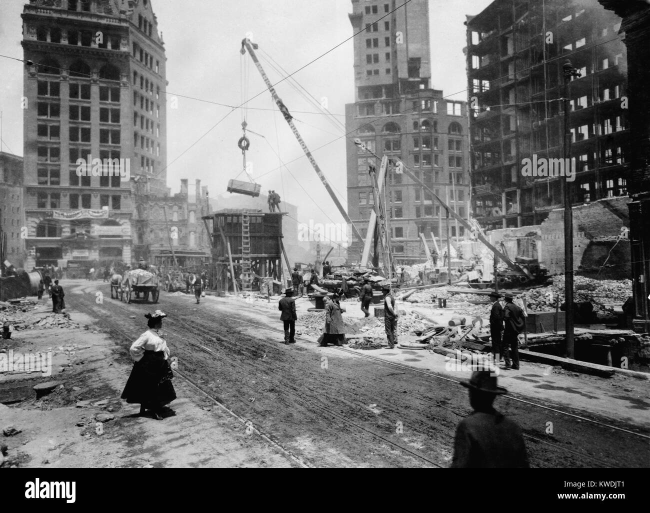 San Francisco rebuilding after the April 18, 1906 earthquake and fire. A crane is moving rubble, as several men and a woman walk by in 1906 (BSLOC 2017 17 52) Stock Photo