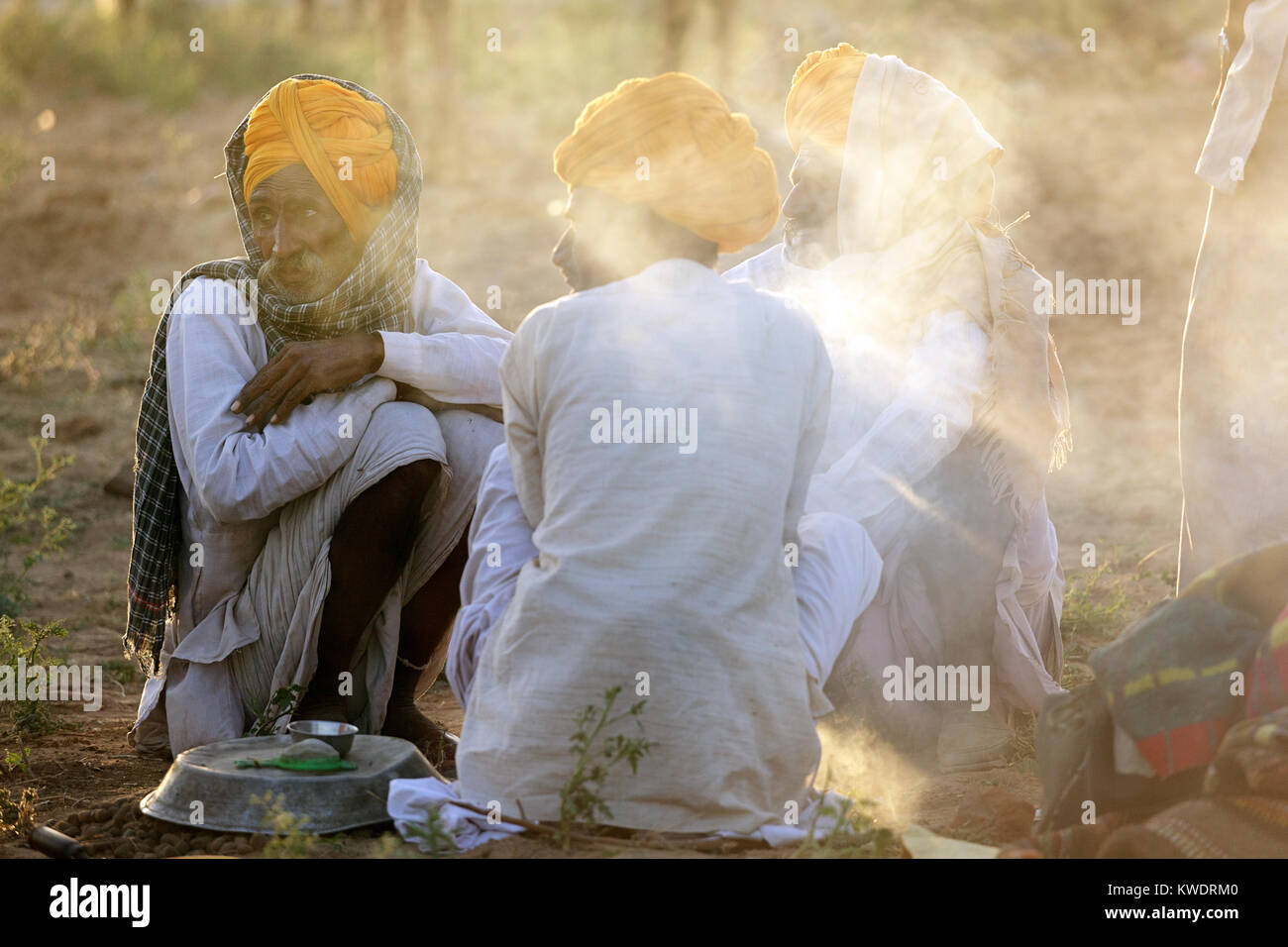 Three traders wearing orange turbans sitting by fireplace at the annual Pushkar Camel Fair, Rajasthan,India. Stock Photo