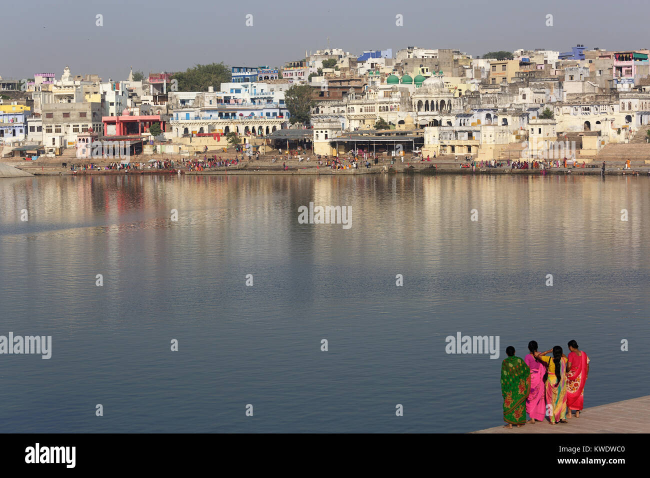 Four indian women in sari standing on the banks of holy lake at Pushkar with Hindu pilgrims taking ritual bath on the opposite side, Rajasthan, India. Stock Photo